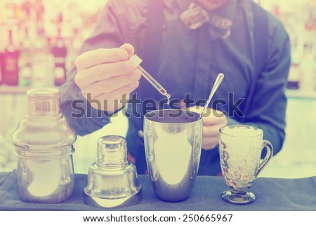Bartender is making cocktail at bar counter, adding some bitter in the shaker, toned image