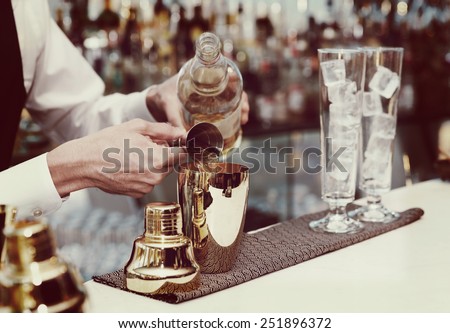 Bartender is pouring liquor in golden shaker, toned image