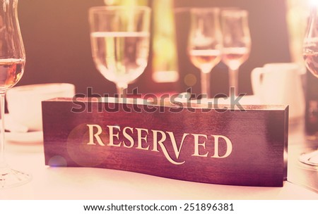 Wooden reserved plate on an arranged restaurant table, toned image
