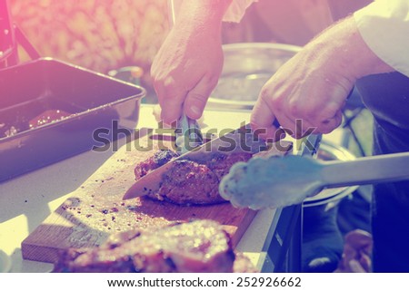 Chef is cutting meat at outdoor kitchen, toned image