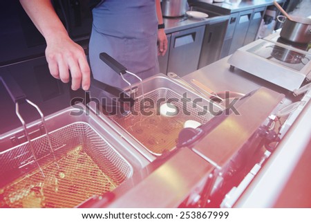 Chef cooking dish in a deep fryer in boiling oil on restaurant kitchen, toned image
