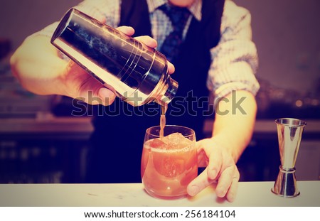 Bartender is making cocktail at bar counter, toned image