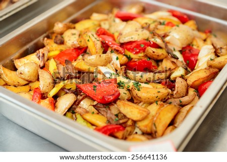 Steel container with roasted potato wedges and vegetables