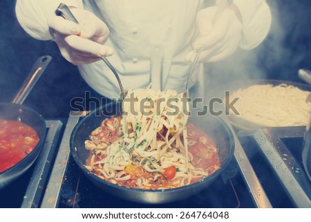 Chef frying mussels with pasta on commercial kitchen, toned image