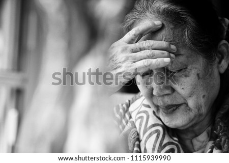 Black and white Image of 60s or 70s  Asian elderly woman facepalm or cover her face by her hands .She may had Headache Symptoms.She looks pain or sick or crying.Sad elderly concept.