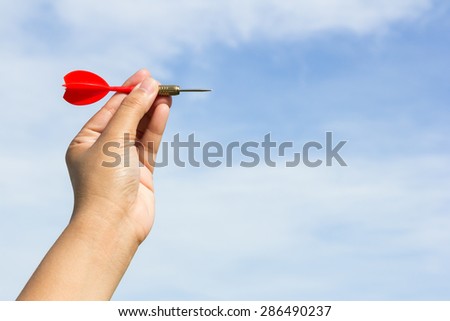 Hand holding red dart on sky background