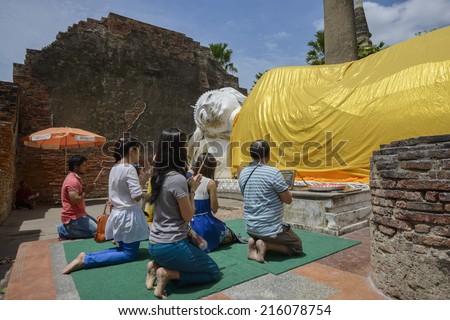 Ayutthaya, Thailand - AUGUST 3, 2013: Unidentified Asian Buddhist family praying and making offerings in front of Buddhist shrine at ancient temple in Thailand\'s former capital, Ayutthaya.