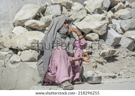 LEH, INDIA - AUGUST 11 2014: An unidentified poor woman begs for money from a passerby in Leh. Poverty is a major issue in India