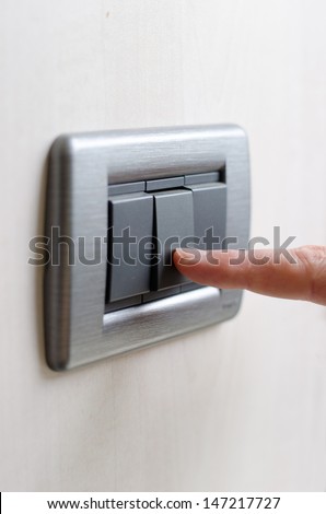 Closeup of finger pressing light switch on the wall, turning lights on or off