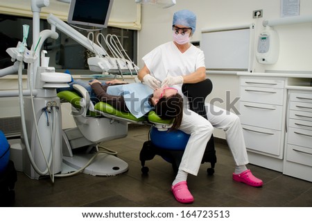 Dentist sitting on ball chair working on patient in dental clinic