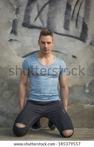 Young man with t-shirt and ripped black jeans kneeling on concrete floor