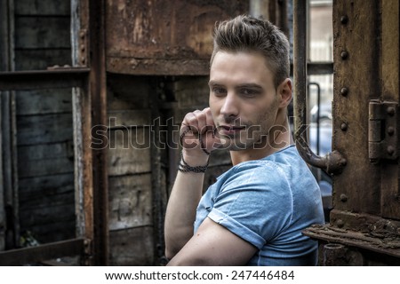 Young man sitting against old rusty train. Looking at camera