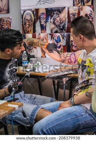 ROME - MAY 11: Tattoo artist draws with his tattoo machine on client\'s arm Virgin Mary\'s face in his workshop on May 11, 2014 in Rome