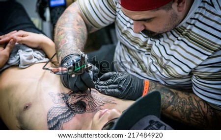 ROME, ITALY - MAY 11: Tattoo artist draws with his tattoo machine on client\'s chest a new design in his workshop on May 11, 2014 in Rome, Italy.