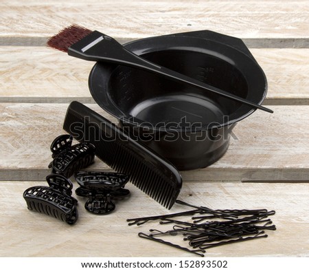 Hair color brush, and bowl with comb, hair clips and pins on wooden surface