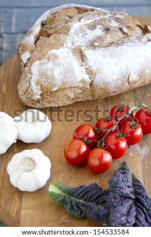 Rye bread, fresh tomatoes, leaves and garlic on a wooden chopping board