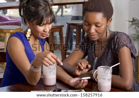 Girlfriends having drink at a coffee shop playing on a phone
