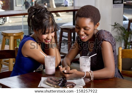Girlfriends having drink at a coffee shop playing on a phone