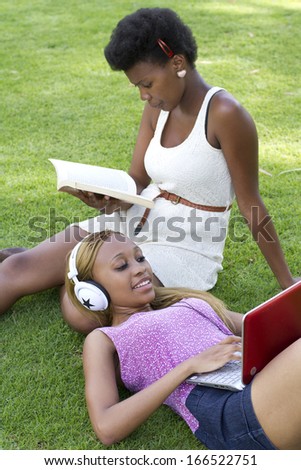 Good looking black females on the grass reading and working on a laptop