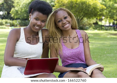 Beautiful black woman on grass with a book and a laptop
