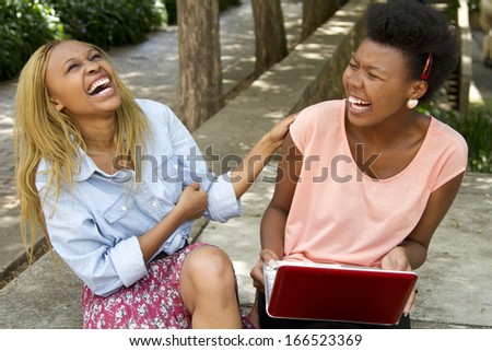 Gorgeous black females sitting outside with a laptop laughing