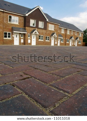 Row of new red brick terraced houses with cobbled pavior street in foreground, UK.