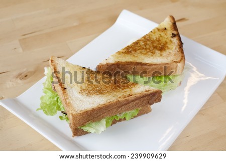 Toasted sandwich with cheese, lettuce, egg and ham on white dish.