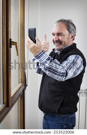 Mature man does ok signal while taking a picture with mobile phone