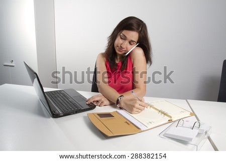 Middle aged woman taking notes on the phone and working with computer