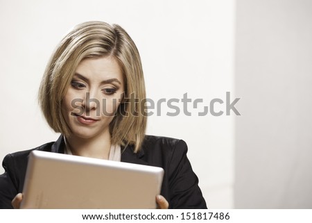 A smart looking young woman looks intently at a digital tablet. She is wearing a business jacket.