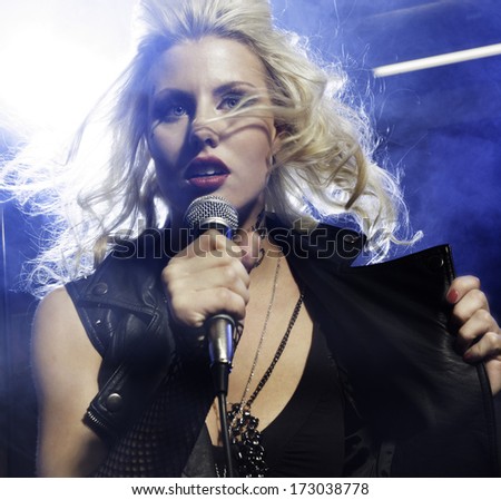 An attractive young woman sings on a stage with lights shining through smoke behind her./Female vocalist