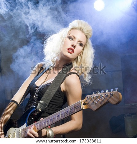 An Attractive Young Woman Plays Guitar On A Stage With Lights Shining Through Smoke Behind Her./Female Musician