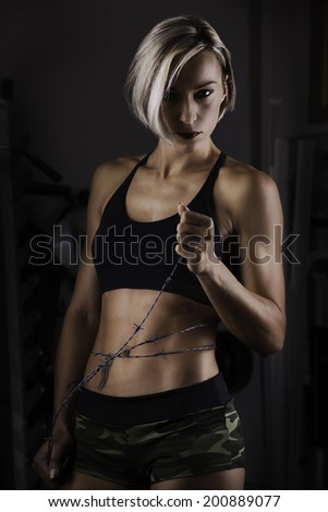A woman with muscle definition is wrapped in barbed wire