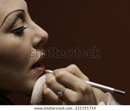 A make up artist puts lip liner on a face for a film noir shot.