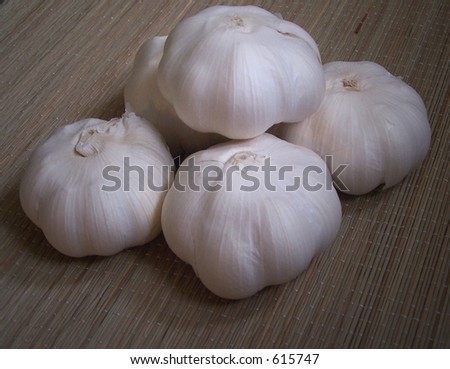 Whole garlic stacked on a natural straw surface in dim light. warm and natural.