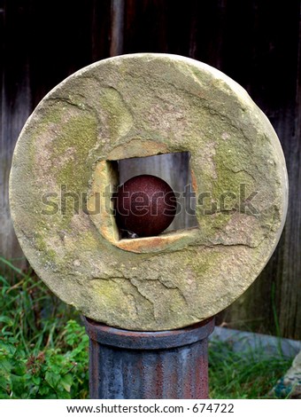 Grindstone on a rusty pedestal, with an old cannon ball in center.