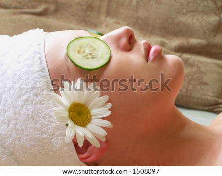 Beautiful woman lying down with cucumber slices and daisy.