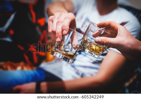 Two hands clink glasses of whiskey at home,on the couch, cozy