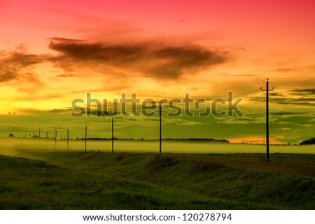 Electricity pylons and lines at dusk over the highway in fog