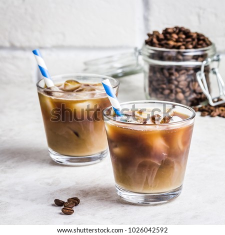 Summer drink iced coffee in glass and coffee beans in glass jar on white background. Selective focus, copy space.