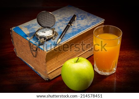 Still life book with pen,watch apple and orange juice.
