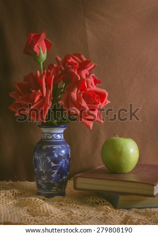 Vintage filtered rose in vase with apple and books.
