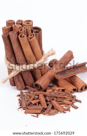 Group of cinnamon sticks on white surface, one in the foreground with ground cinnamon and two packets in the background.