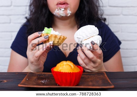 Food addiction, dieting concept. Young overweight woman fed up with diets eating a cake greedily, staining  face in cream.