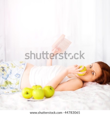 beautiful woman eat apple and reading book in bed