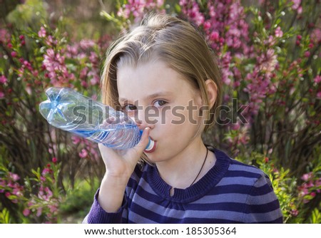 Little schoolgirl  drinks water from a plastic bottle outdoors in spring