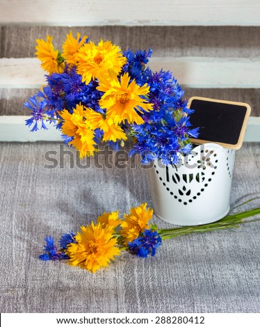 Composition with blue and yellow colors of wild flowers in a decorative vase with tablet for text