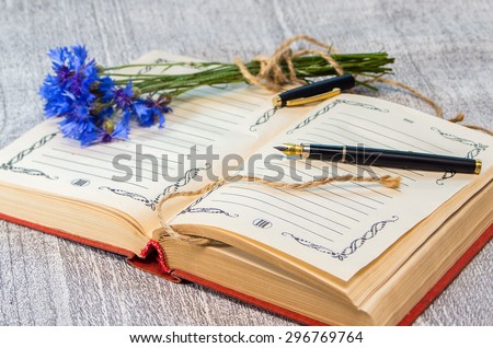 open book with pen and blue cornflowers in the background. Intentional blur.