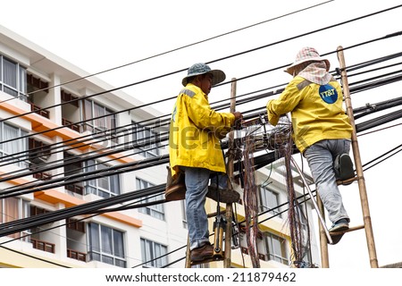 PHUKET, THAILAND - AUGUST 20 : Two male workers on bamboo ladders are repairing a telephone line on August 20, 2014 in Phuket Thailand.