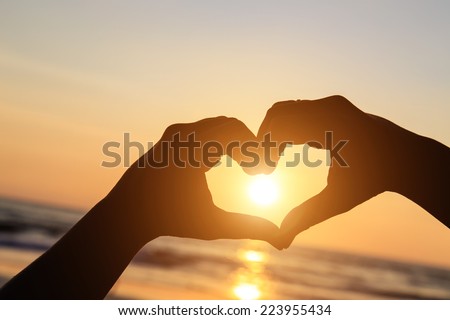 Silhouette of hands in heart  symbol around the sun